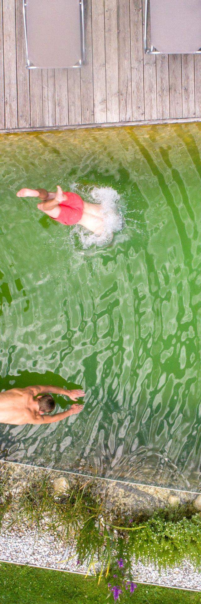 Menschen entspannen und tauchen in einen Naturpool mit grünem Wasser und Holzdeck