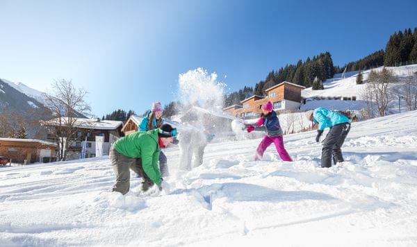 Kinder spielen im Schnee während Winterurlaub bei Alpenchalets an sonnigem Tag
