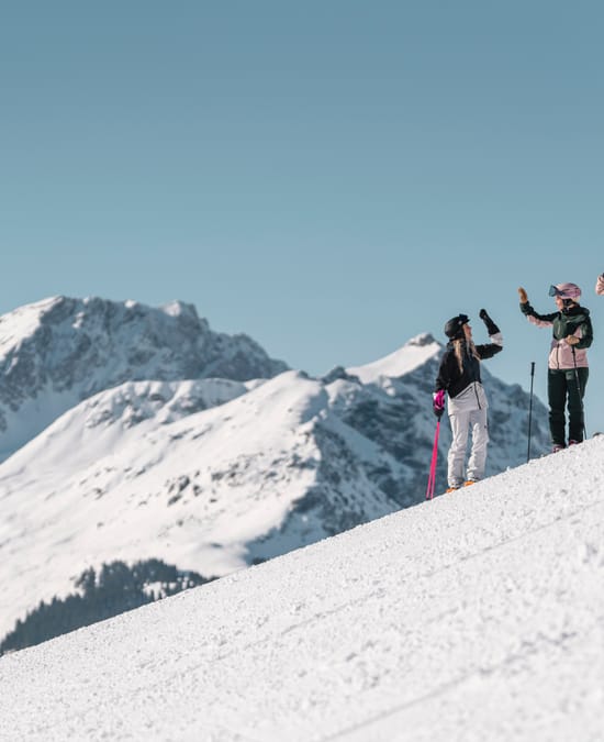 3 Frauen beim Skifahren, Klatschen mit den Händen ein. Im Hintergrund Tief verschneite Berge 