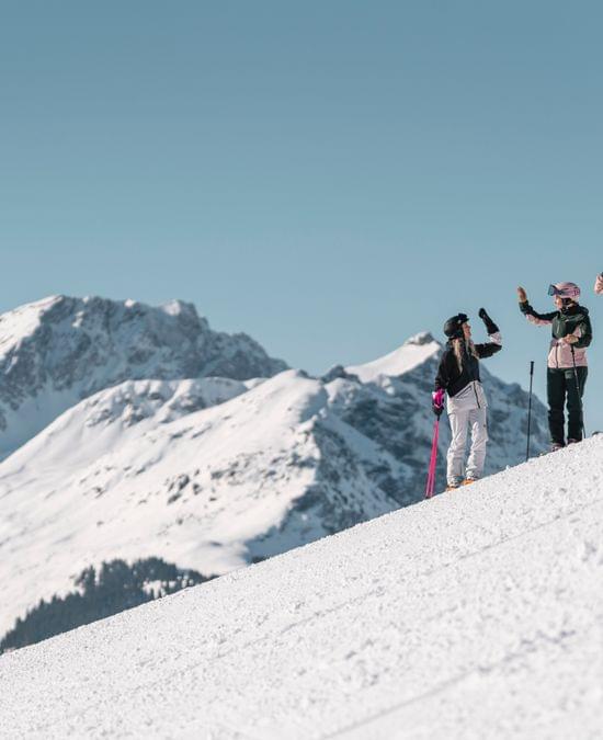3 Frauen beim Skifahren, Klatschen mit den Händen ein. Im Hintergrund Tief verschneite Berge 