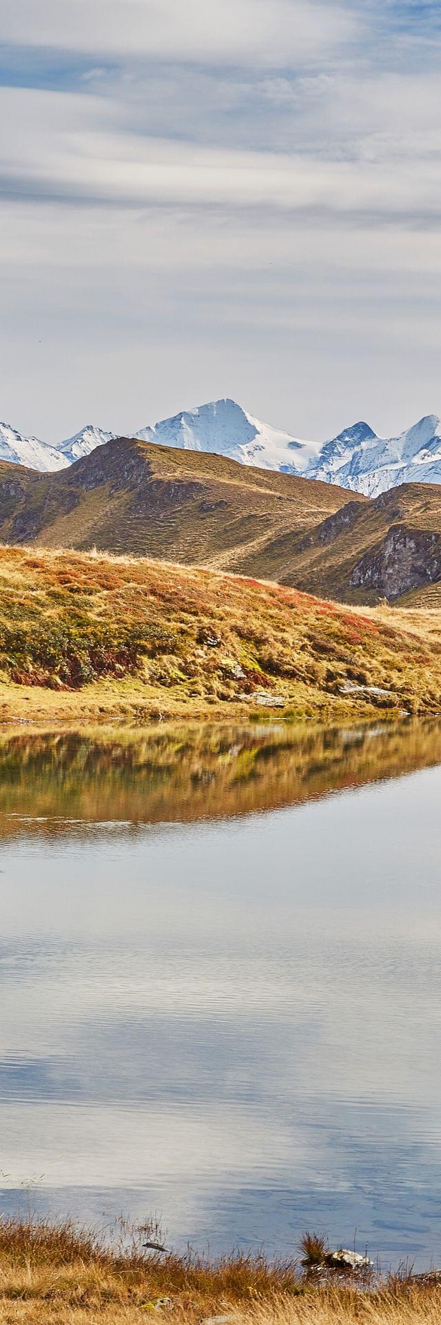 Alpine lake reflecting mountain peaks under a partly cloudy sky in autumn