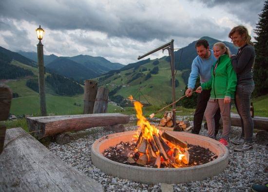 Familie röstet Marshmallows über Lagerfeuer in malerischer Berglandschaft