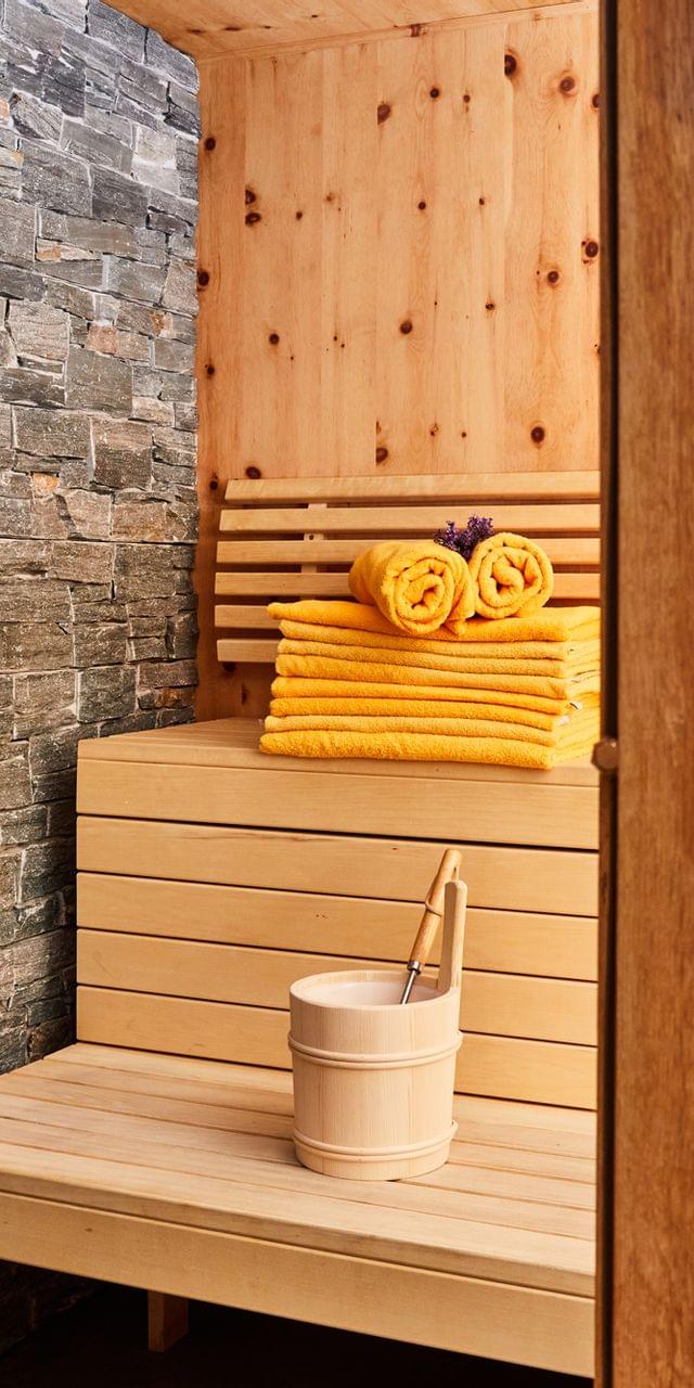 Moderner Holzsauna-Innenraum mit gestapelten gelben Handtüchern und Saunakübel