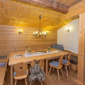 Gemütliches alpines Esszimmer aus Holz mit Kronleuchter, rustikalen Möbeln und angrenzendem Schlafzimmer