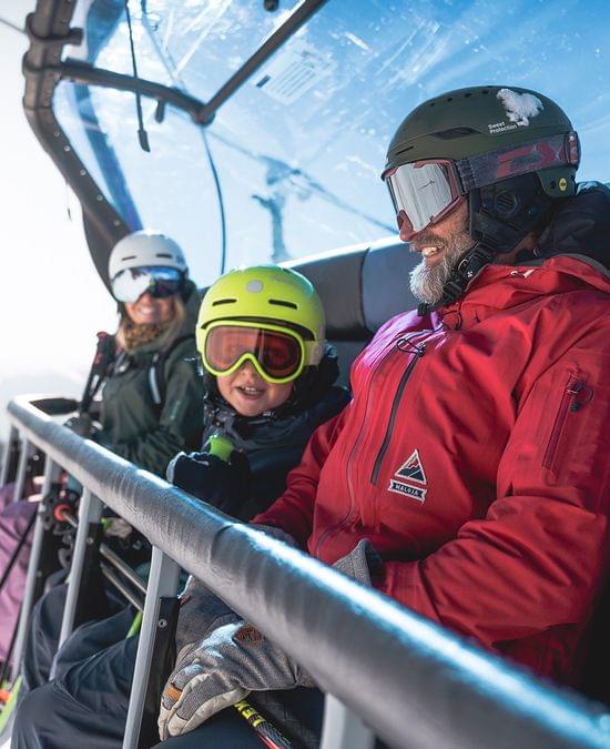 Familie in Skibekleidung fährt an einem sonnigen Wintertag mit dem Sessellift