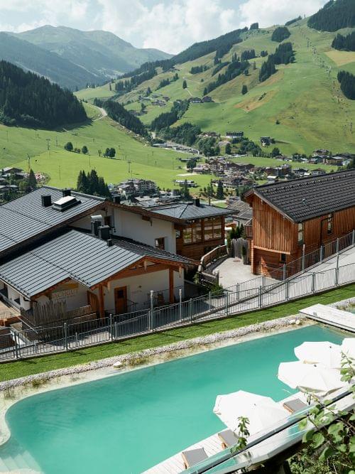 Luxuriöses Alpendorf mit Pool und Holzhütten mit Blick auf das Bergtal im Sommer