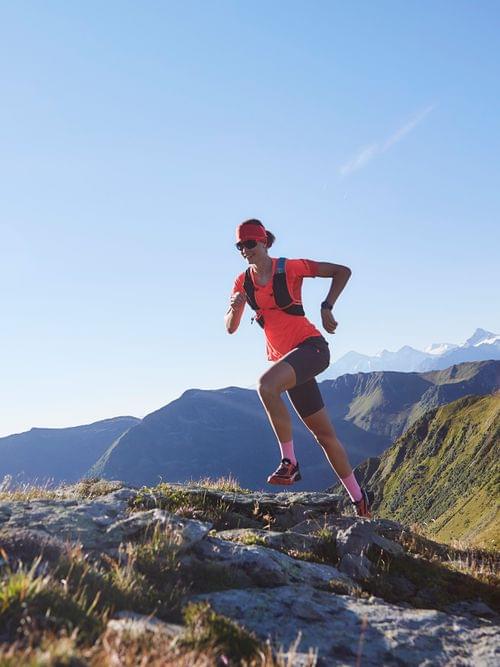 Trail runners climbing a rocky alpine path with mountain peaks in the background