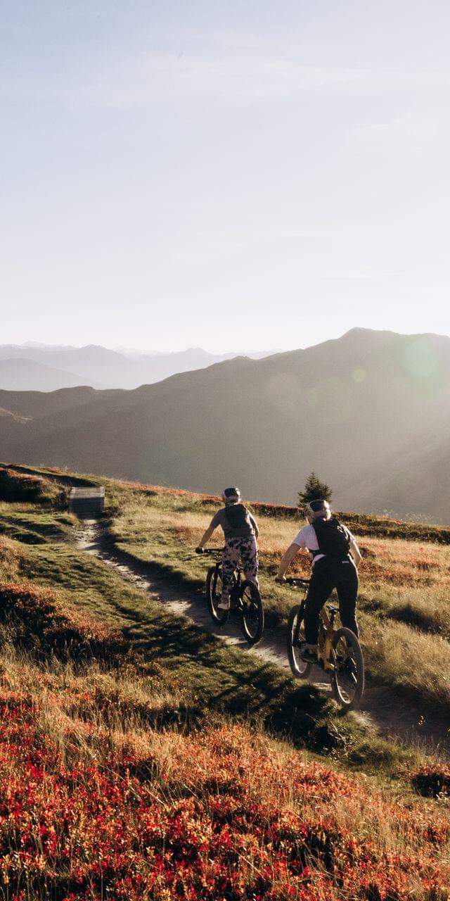 An atmospheric view of the autumn mountain landscape, with two mountain bikers riding down a trail.