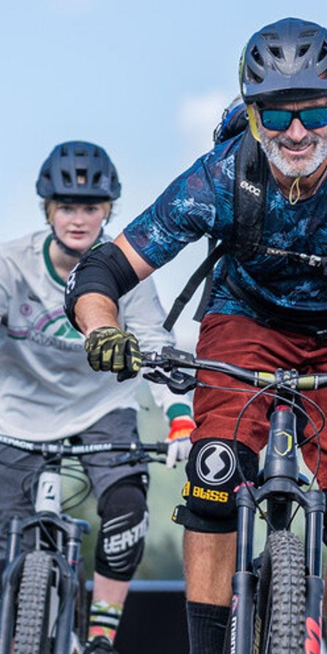 Zwei Mountainbiker fahren einen Trail in alpiner Landschaft hinunter