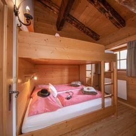Gemütliches Schlafzimmer in Holzhütte mit Etagenbett, rot karierten Bettdecken und rustikaler Alpendekoration