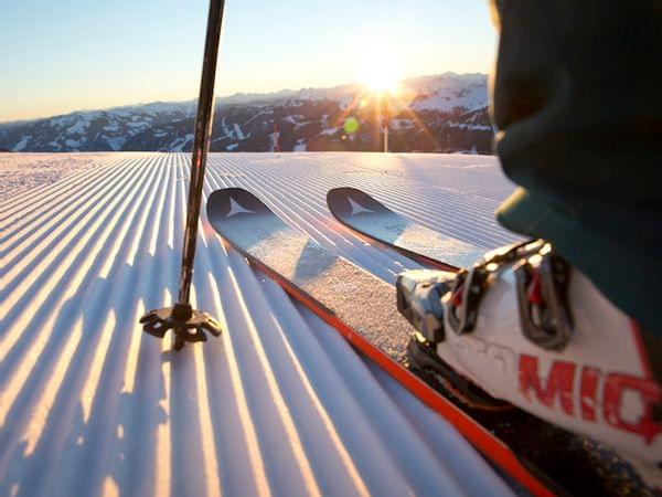 Skifahrer mit Skischuhen und Stöcken auf frisch präparierter Piste bei Sonnenaufgang