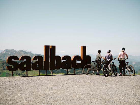 3 Mountainbiker am Berg, stehen vor einem Großem Saalbach Schild 