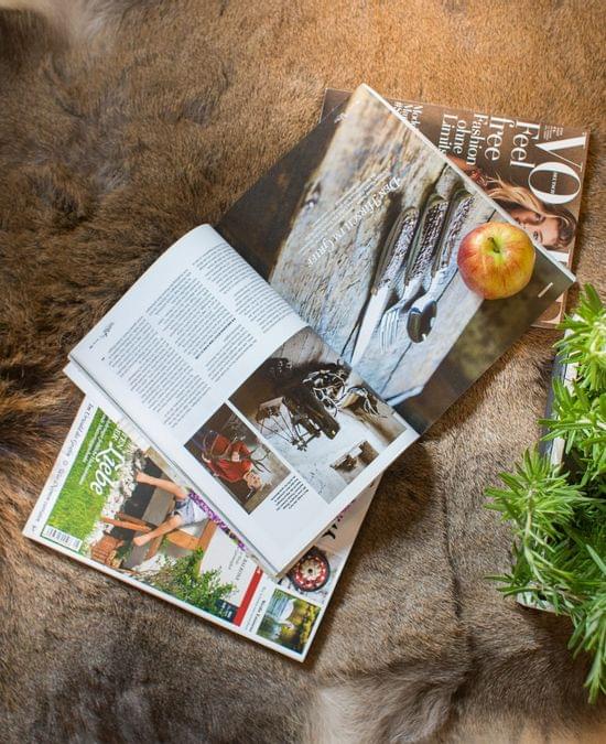 Zeitschriften, ein Apfel und ein Holzkasten mit Kräutern auf einem Fellteppich mit Holzboden