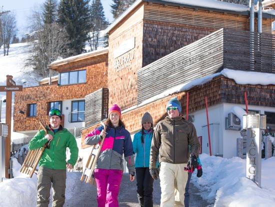 Gruppe in Winterkleidung mit Schlitten vor Alpenlodge im verschneiten Bergresort