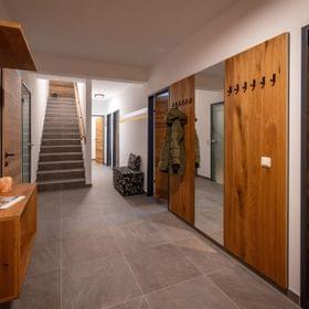 Modern hallway with wooden coat hangers, stone floor tiles and staircase leading upstairs