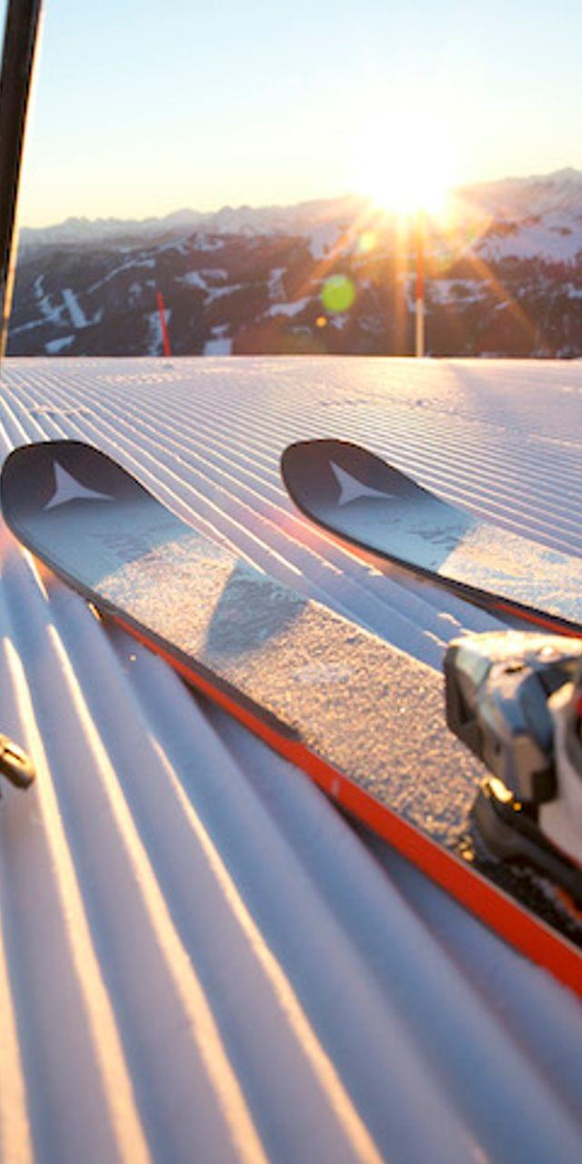 Skifahrer mit Skischuhen und Stöcken auf frisch präparierter Piste bei Sonnenaufgang