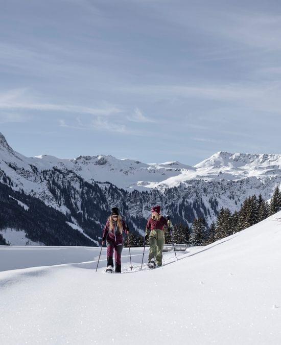 Zwei Frauen beim Schneeschuhwandern im Tiefschnee vor alpiner Bergkulisse
