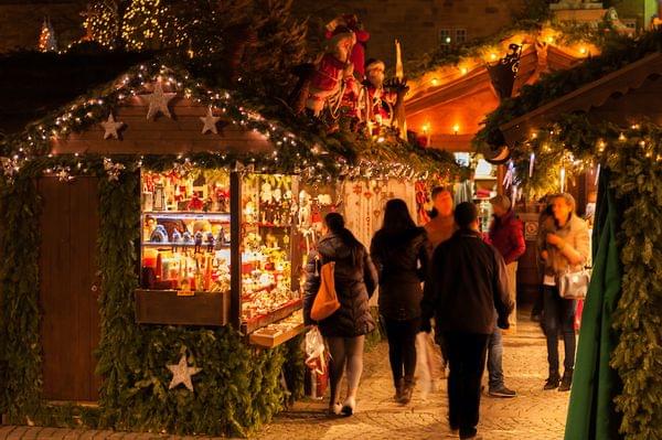 Menschen kaufen an geschmückten Weihnachtsmarktständen mit Lichtern und Festdekorationen ein