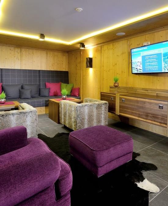 Gemütliche Alpenlounge mit lila Sesseln, fellbezogenen Hockern und Wandfernseher