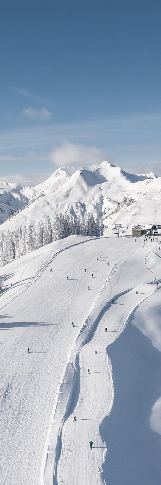 Ski resort with snow-covered slopes, chairlifts, and alpine mountains under clear blue sky