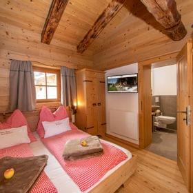 Cozy alpine bedroom with wooden interior, red checkered bedding, and en-suite bathroom