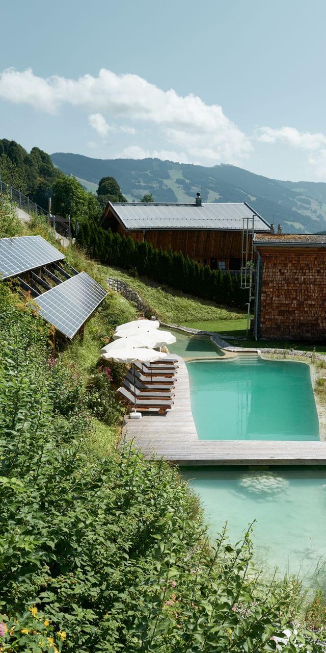Umweltfreundlicher Naturpool mit Liegen und Solarpanels in alpiner Berglandschaft