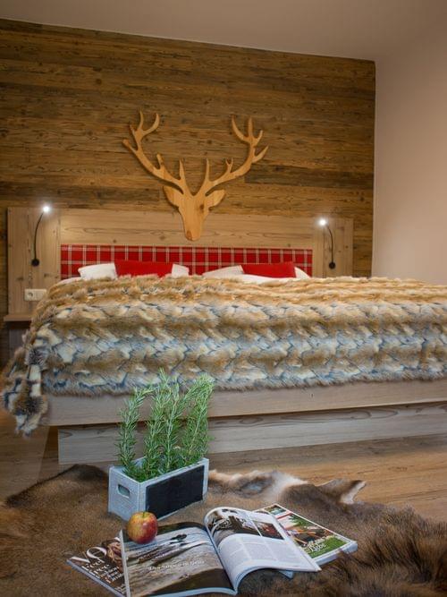 Gemütliches Alpen-Schlafzimmer mit Kunstfelldecke, Hirschkopf aus Holz und rustikaler Dekoration