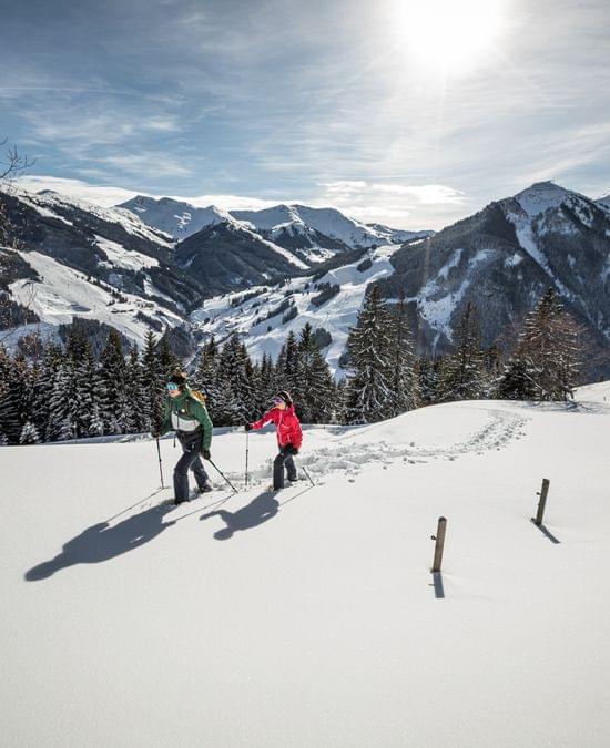 Two women winter hiking through a snow-covered mountain landscape.