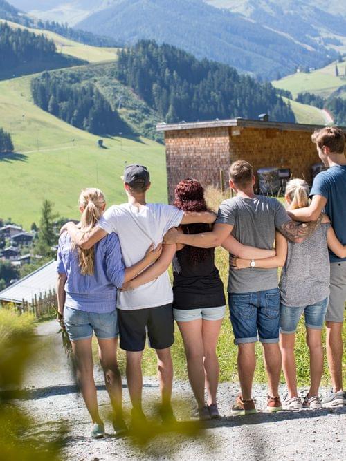Freundesgruppe steht Arm in Arm auf Bergpfad mit Blick auf Alpenort