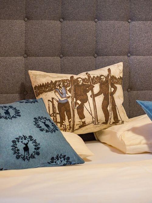 Gemütliches Hotelbett mit blauen Kissen mit Hirschmotiv und Vintage-Skifahrer-Kissen