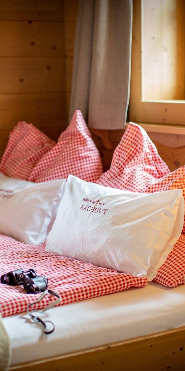 Gemütliches Alpenzimmer mit rotkariertem Bett, Wanderkleidung und Fernglas auf der Matratze