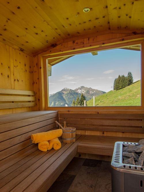 Wooden sauna interior with mountain view through large window and folded towels on bench