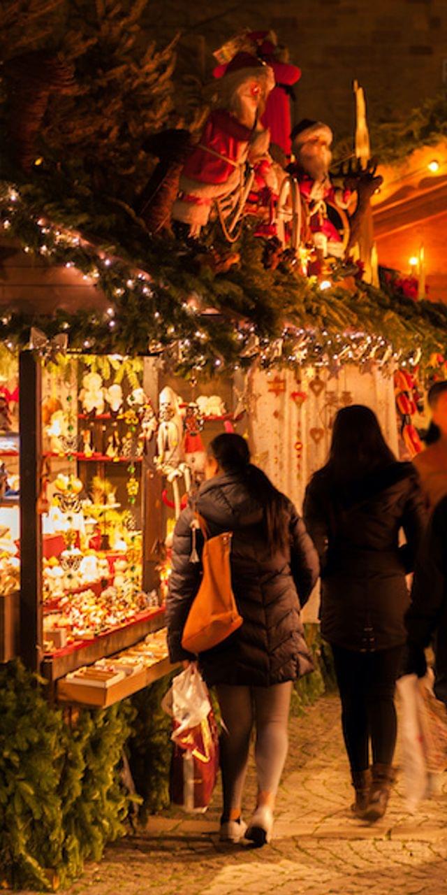 Menschen kaufen an geschmückten Weihnachtsmarktständen mit Lichtern und Festdekorationen ein