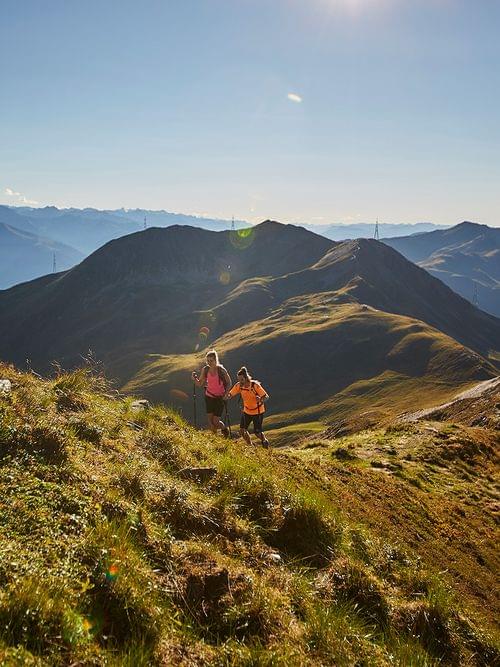 Two hikers trekking on a sunny mountain trail with panoramic alpine views