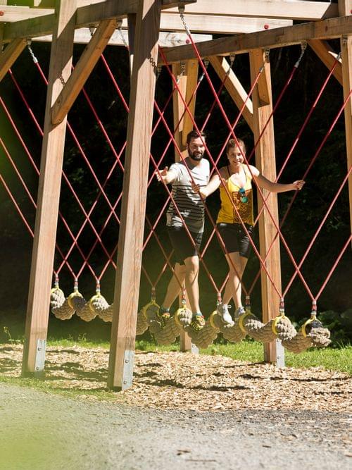 Two people balancing on rope swings in outdoor adventure park