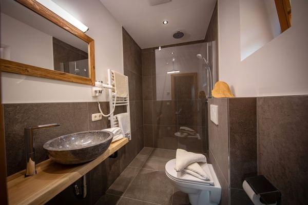 Modernes Badezimmer mit Steinschüsselwaschbecken, Wandspiegel, begehbarer Dusche und Handtüchern auf der Toilette