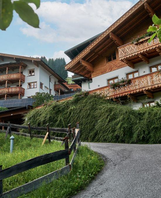Charming Alpine hotel with wooden balconies surrounded by greenery and a curved mountain road