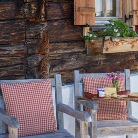 Rustikale Holzstühle mit karierten Kissen und Alpenfrühstück auf Tablett vor Hütte