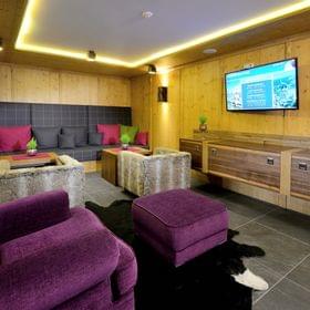 Gemütliche Alpenlounge mit lila Sesseln, fellbezogenen Hockern und Wandfernseher