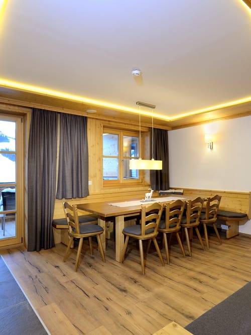 A kitchen with a dining area, featuring a large table with a corner bench and chairs, in a cozy alpine-chic style.