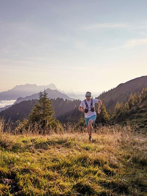 Trailrunner in alpiner Landschaft bei Sonnenaufgang mit Bergblick und grasigem Hang