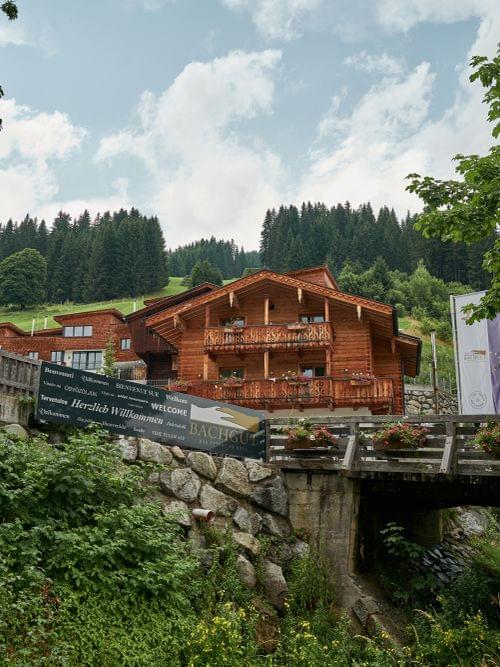 Traditionelles Alpenhaus mit Holzbalkonen, umgeben von Wald und Berglandschaft
