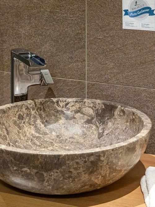 Modernes Bad mit steinernem Waschbecken, Chromarmatur und gerollten weißen Handtüchern