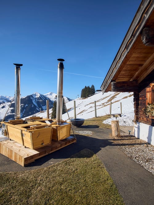 The Bachalm exterior in spring skiing conditions, with two wood-fired outdoor bathtubs in the background.