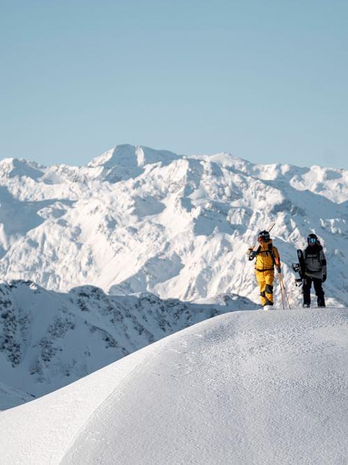 Zwei Skifahrer wandern auf verschneitem Bergrücken mit Alpen im Hintergrund
