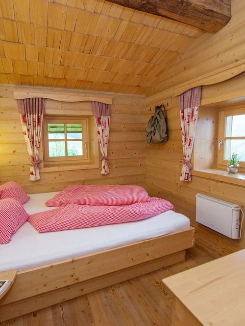 Cozy alpine bedroom with wooden walls, double bed in red checkered bedding, and rustic decor