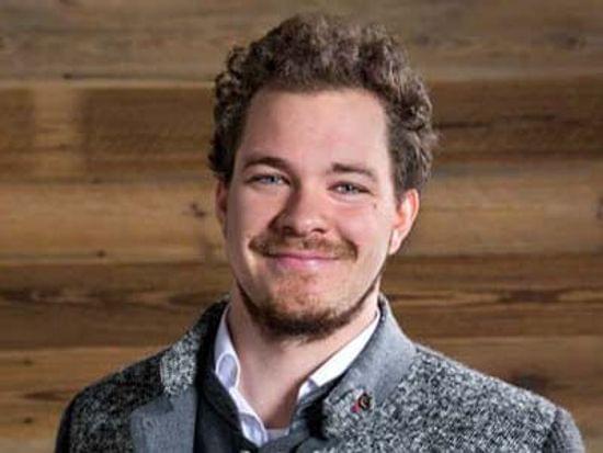 Lächelnder Mann mit Bart im grauen Blazer vor Holzvertäfelung