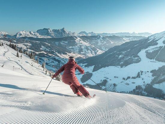 Skifahrer fährt bei Sonnenschein eine frisch präparierte Piste in den österreichischen Alpen hinunter