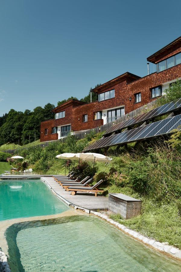 Öko-Hotel mit Holzfassade, Solarpaneelen und Sonnenliegen am Naturpool
