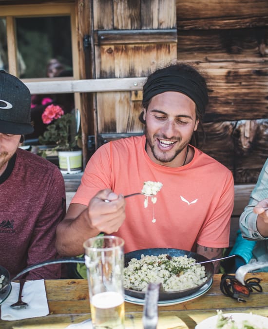 Two men and one woman sitting at a table outside an alpine hut, having lunch.